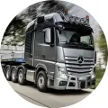 Stříbrný tahač Mercedes-Benz s návěsem betonových bloků jede po silnici, zelené rozmazané pozadí, jedlý obrázek na dort