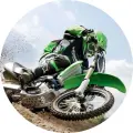 Závodník na zelené motokrosové motorce v prudkém náklonu v zatáčce, za kolem létá hlína, modrá obloha; jedlý obrázek na dort