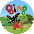 Černý králíček Bing v červených kalhotách skáče v parku vedle oranžového Flopa, v pozadí zelené keře a modrá obloha, jedlý obrázek na dort