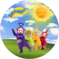 Kulatý jedlý obrázek na dort: čtyři barevné postavičky Teletubbies stojí na zelené louce pod modrou oblohou se žlutým sluníčkem.
