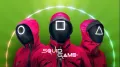 Tři strážci Squid Game v červených oblecích s maskami s kruhem, čtvercem a trojúhelníkem na zeleném pozadí, jedlý obrázek na dort
