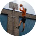 Basketbalista v oranžové mikině skáče s míčem ke koši u cihlové zdi, jedlý obrázek na dort