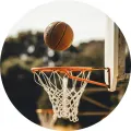 Basketbalový míč mířící do oranžového koše na venkovním hřišti, zelené stromy v pozadí, jedlý obrázek na dort