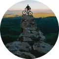 Cyklista s kolem stojící na skalním útesu s horskou krajinou a zelenými kopci v pozadí, jedlý obrázek na dort