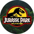 Kruhový emblém s černou siluetou tyranosaura na zeleném pozadí kapradí a žlutým okrajem, jedlý obrázek na dort